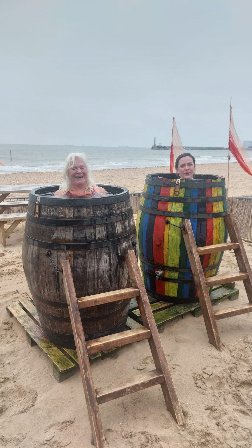 Two retreat guests laughing in barrel plunge pools on the beach — the famous ice bucket